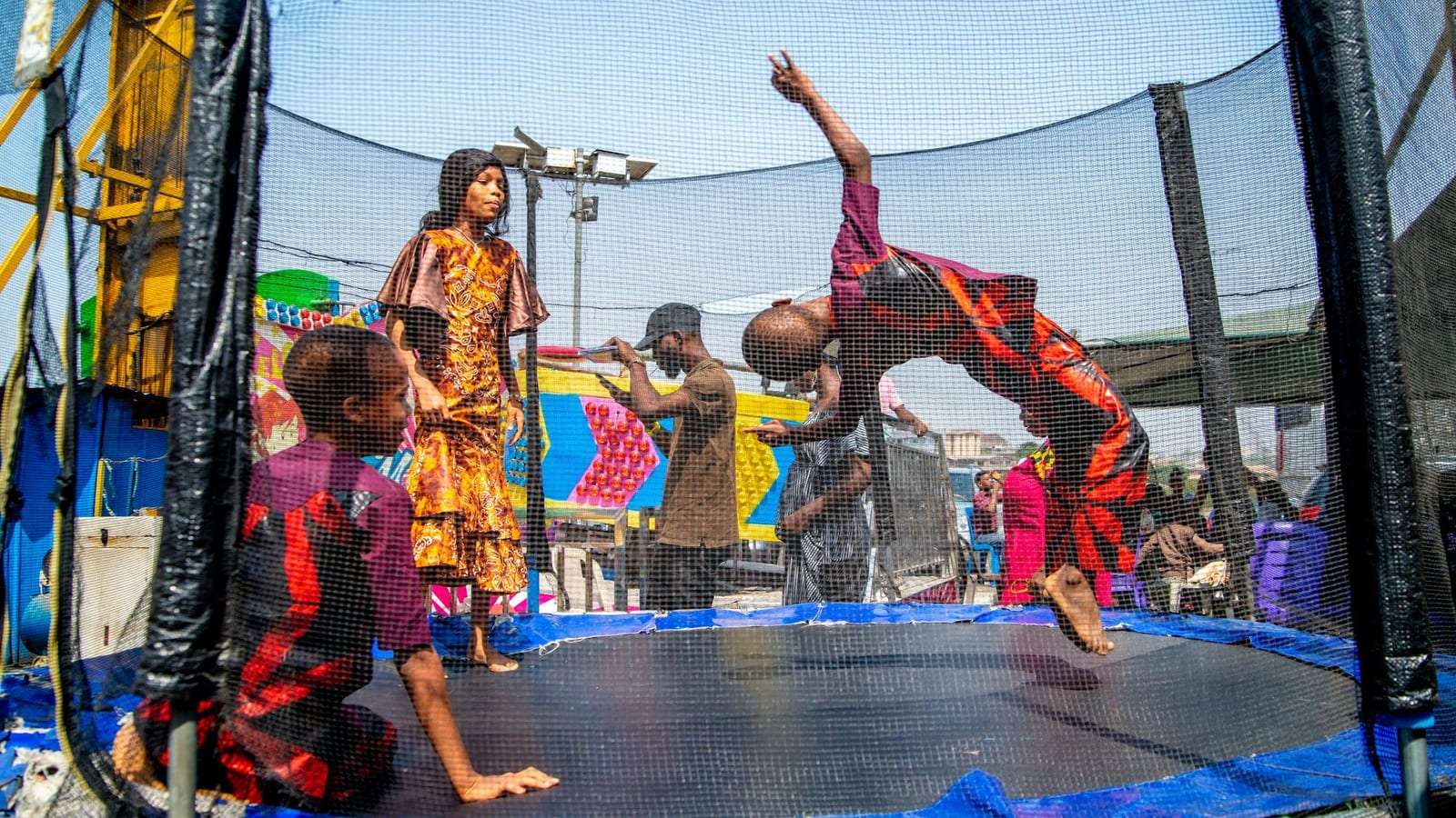 Niños juegan dentro de un trampolín con red: uno da una voltereta hacia atrás y otro está sentado en la lona